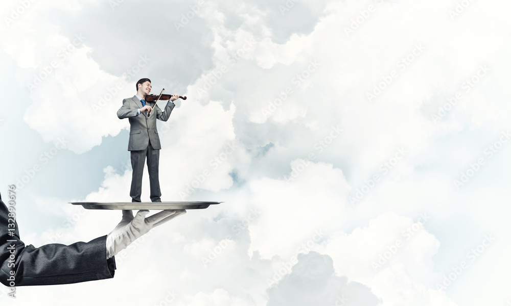 Businessman on metal tray playing violin against blue sky background Businessman on metal tray playing violin against blue sky background