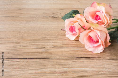 Three beautiful pink roses on brown wooden background with lots of copy space.