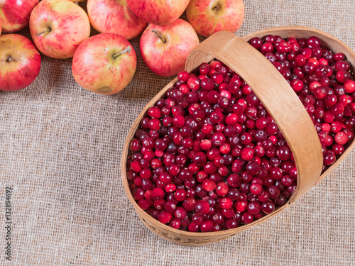 Cranberries in a basket on a fabric background and apples lying next photo