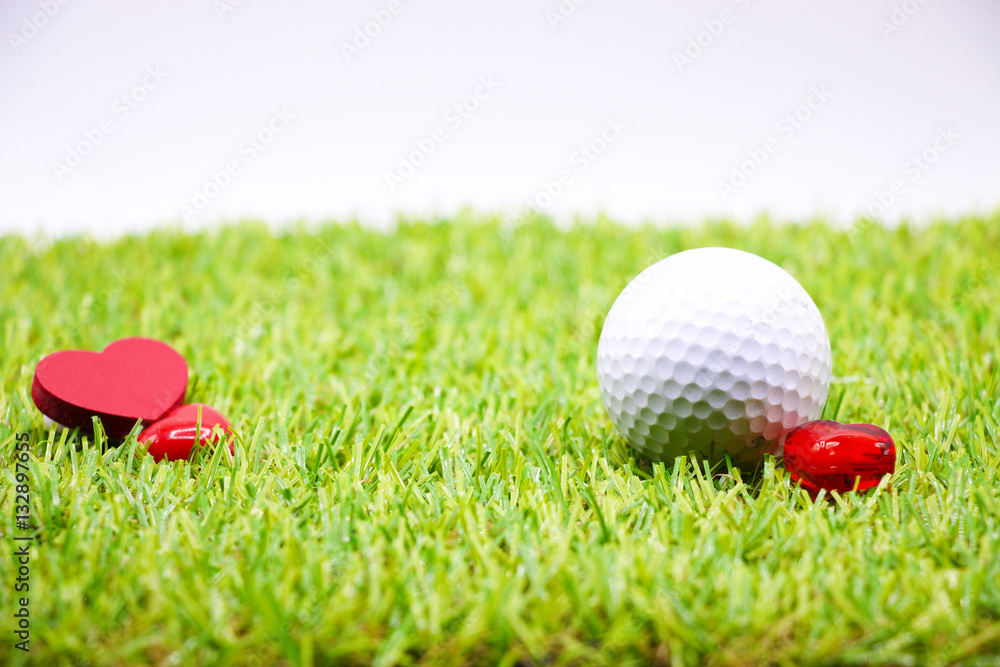 Naklejka premium golf ball and red heart are on green grass