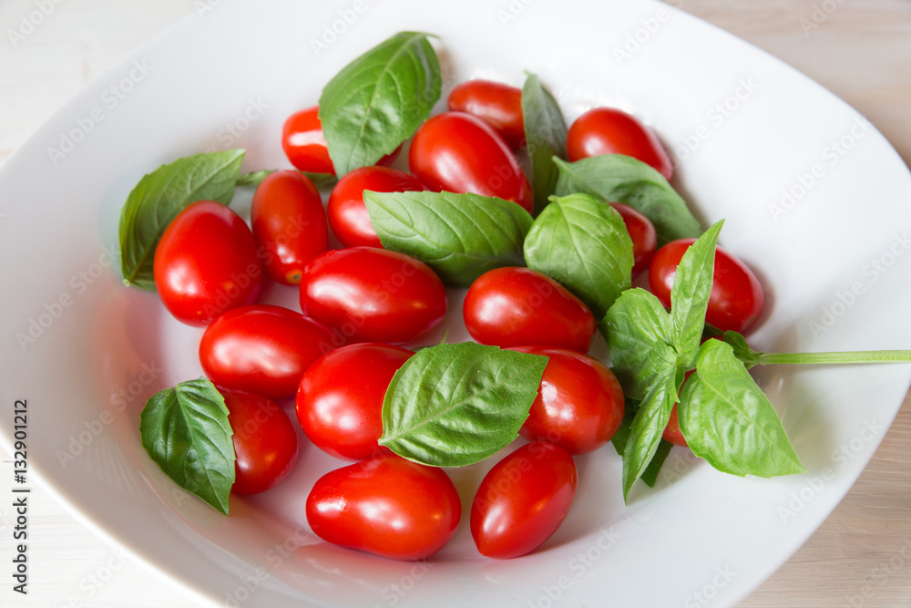 Bowl with fresh red grape tomatoes and green basil leaves Bowl with fresh red grape tomatoes and green basil leaves