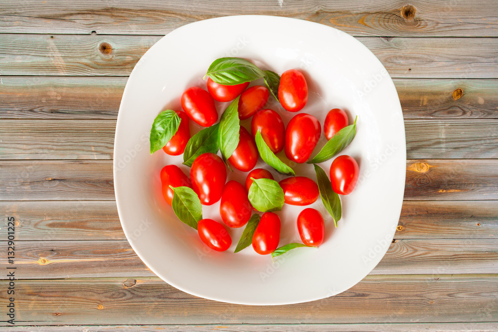 Bowl with fresh red grape tomatoes and green basil leaves