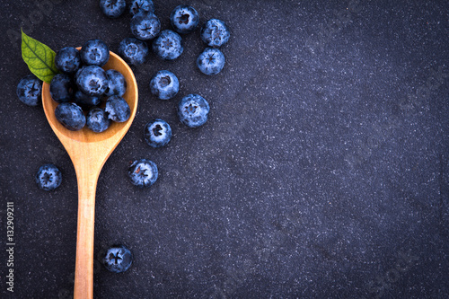 Tela fresh picked blueberries in wooden spoon on black stone