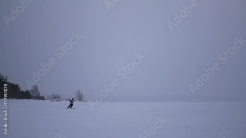 athlete in the winter kite making jumps and lands on a frozen lake in the snow near the shore, slow motion photo