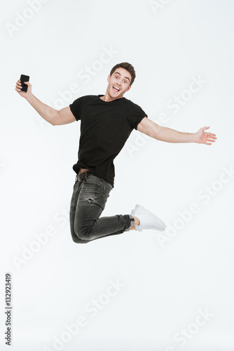 Happy young man jumping over white background holding phone.