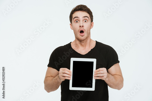 Young shocked man showing display of tablet computer.