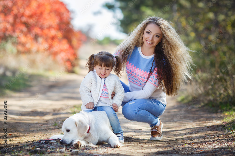 Family portrait of young blonde woman with long wavy hair and her little daughter,walking together with the dog breed Golden Retriever in a beautiful autumn Park