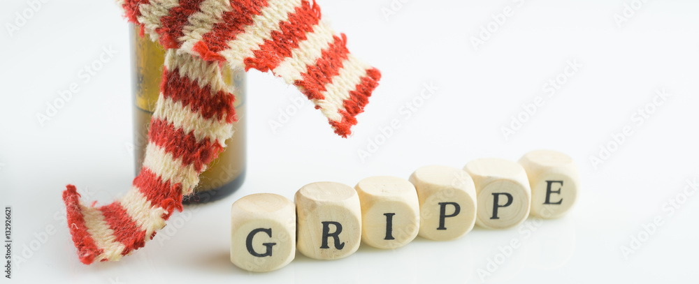 Das Wort Grippe mit kleinen Buchstabenwürfeln aus Holz und einem Arzneifläschchen mit Schal auf weißem Hintergrund Das Wort Grippe mit kleinen Buchstabenwürfeln aus Holz und einem Arzneifläschchen mit Schal auf weißem Hintergrund