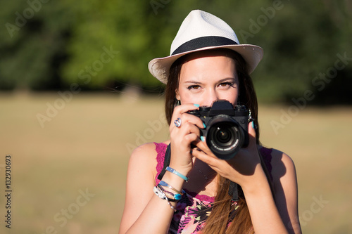 beautiful brown hair girl with white panama hat while shooting a picture with her camera at park in a sunny day. summer portrait