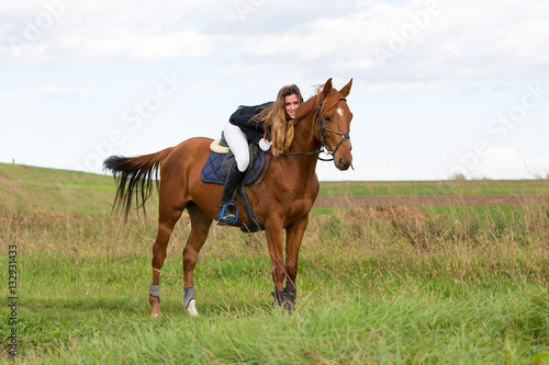 Beautiful young girl in uniform competition ride and stroke her brown horse : outdoors portrait on sunny day