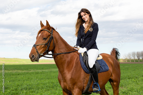 Beautiful young girl in uniform competition rides with safety her brown horse and smiling: outdoors portrait on sunny day