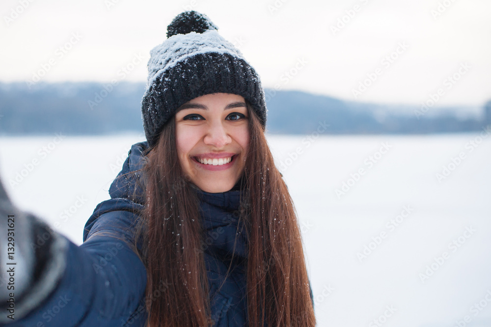 Young beautiful woman taking selfie photo in winter snow park near frozen lake Young beautiful woman taking selfie photo in winter snow park near frozen lake