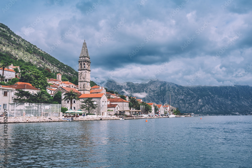 Famous ancient Perast village on Kotor bay by cloudy day in Montenegro. View to Perast Old Town roofs and mountains from water of Boka Kotorska. Postcard montenegrin landscape.
