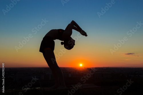 Silhouette of sporty woman practicing yoga in the park at sunset - drop back  wheel pose. Sunset light  sun lens flares  golden hour. Freedom  health and yoga concept