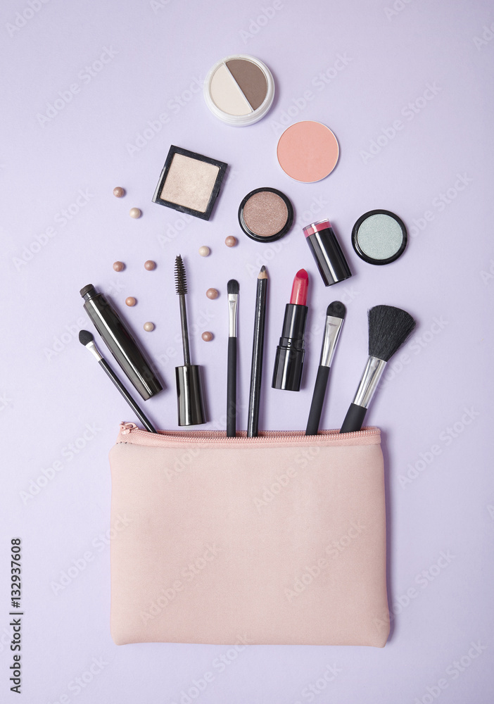 Aerial view of a pink make up bag, with cosmetics spilling out on to a pastel purple background Aerial view of a pink make up bag, with cosmetics spilling out on to a pastel purple background