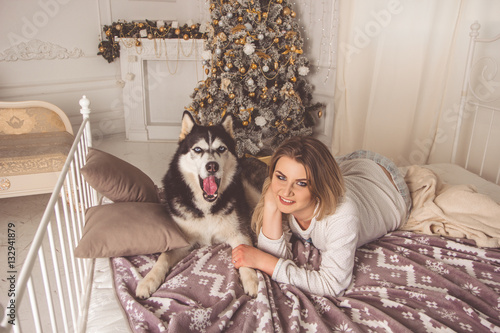 Girl with husky dog in bed near Christmas tree