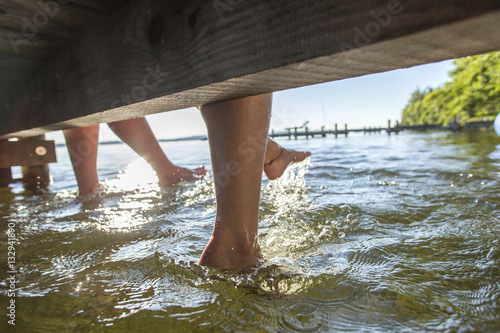 Young women sit on pier bathing feet in water photo