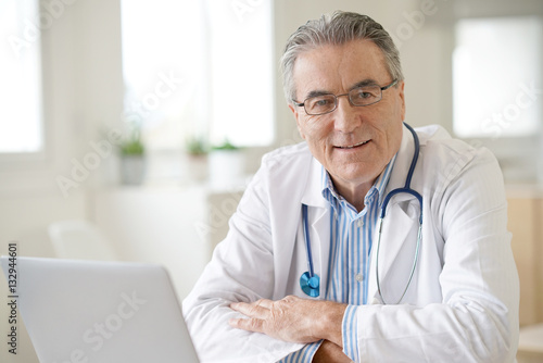 Portrait of senior doctor sitting in medical office photo