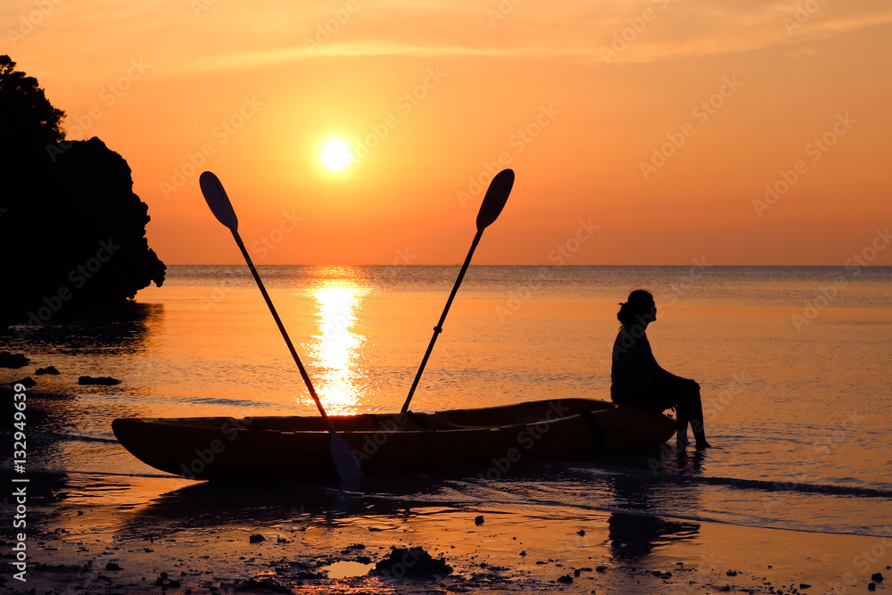 Woman sitting on a kayak on the beach at sunset. 