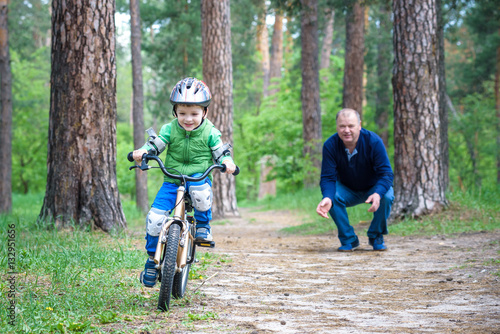 Little kid boy of 3 years and his father in autumn forest with a bicycle. Dad teaching son. Man happy about success. Child helmet. Safety, sports, leisure kids concept