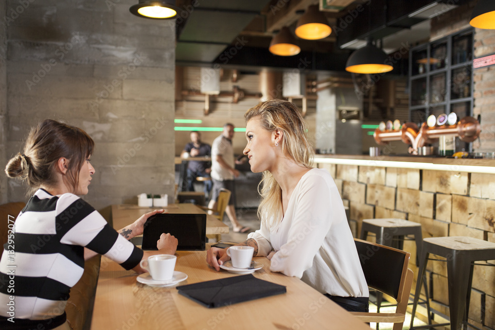 Two girlfriends in coffee shop looking at digital tablet Two girlfriends in coffee shop looking at digital tablet