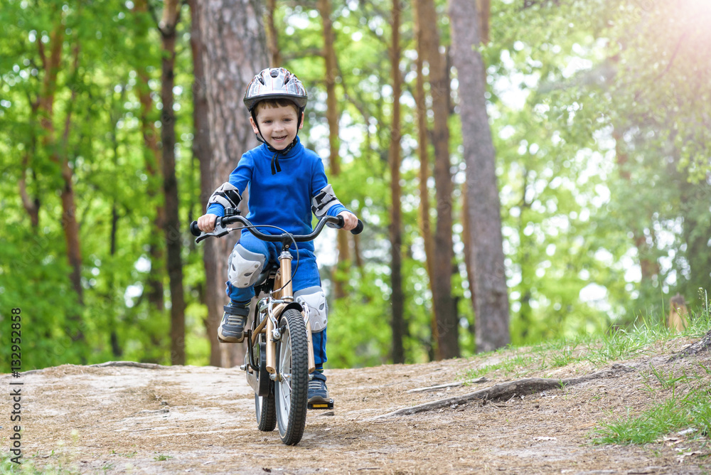 Happy funny little kid boy in colorful raincoat riding his first bike on cold day in forest. Happy funny little kid boy in colorful raincoat riding his first bike on cold day in forest.