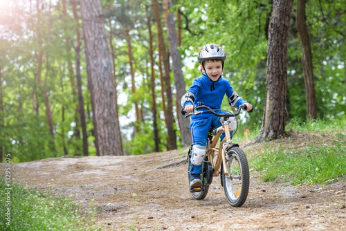 Happy cute blond kid boy having fun his first bike on sunny summer day, outdoors. child making sports. Active leisure for children. wear safety helmet. is smiling and cicling.