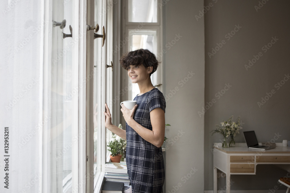 Portrait of smiling young woman looking through window at home Portrait of smiling young woman looking through window at home