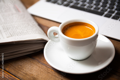 Cup of espresso with laptop and newspaper on wooden desk