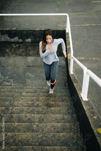 Latin urban fitness woman running and climbing stairs for legs power and strength training. Female athletes working out outdoor in rainy winter day. © Dirima