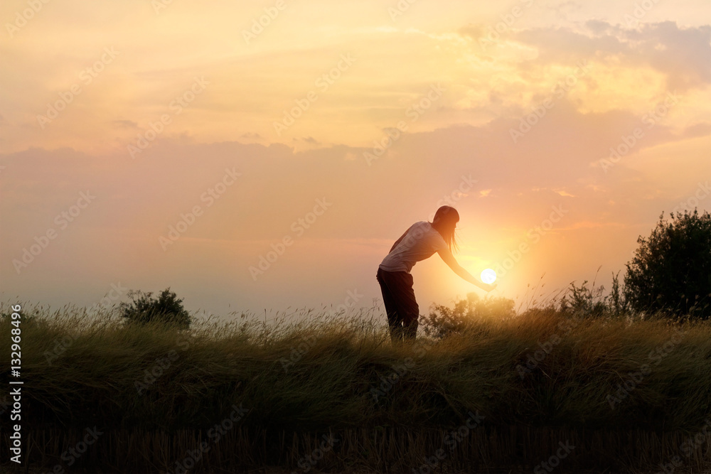 Silhouette of woman reaching hand to the sun in beautiful field, sunset background