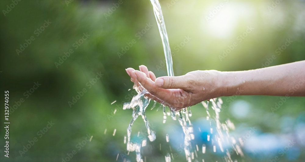 Water pouring in woman hand on nature background, environment concept - obrazy, fototapety, plakaty 