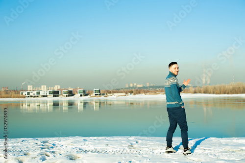 man in warm sweater with a beard is walking on the street in the winter in a warm sunny day at the river against the backdrop of the city, laughing at the problem of the environment and emissions