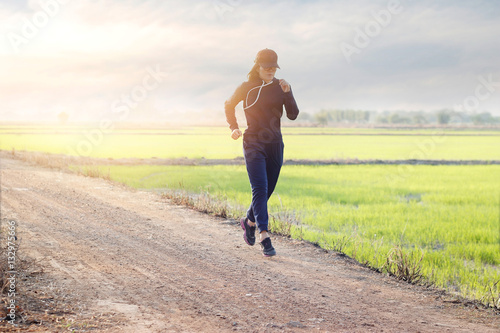 woman running excercise on rural road of green field sunset background
