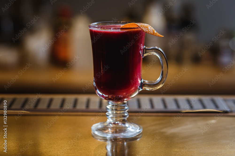 A transparent cup of raspberry mulled wine with orange peel on a bar stand. Selected focus, small depth of field, film grain effect. A transparent cup of raspberry mulled wine with orange peel on a bar stand. Selected focus, small depth of field, film grain effect.