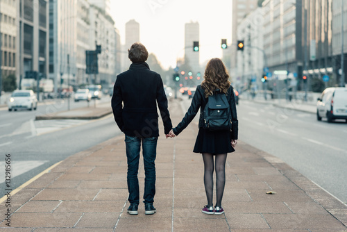 Back view of young beautiful couple in love hand in hand walking outdoor in the city, having fun - first date,  romantic, love concept