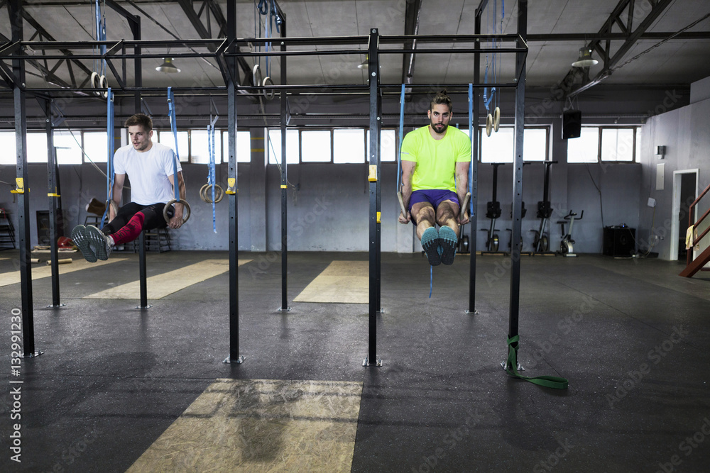 Two men doing gym exercise on rings in gym Two men doing gym exercise on rings in gym