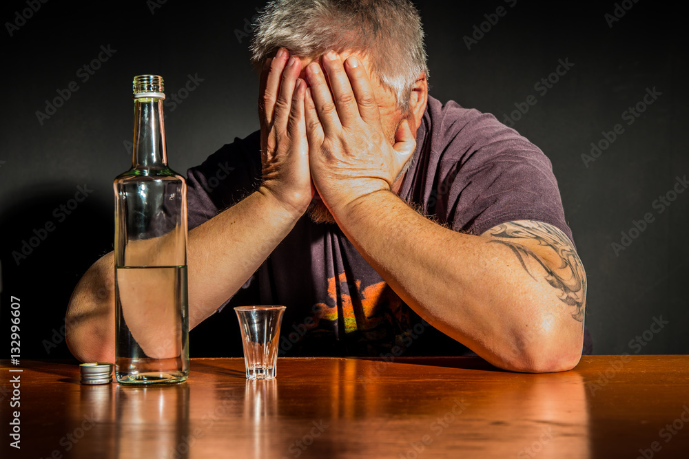 ein Mann sitzt mit einer Flasche Alkohol an einem Tisch - obrazy, fototapety, plakaty 
