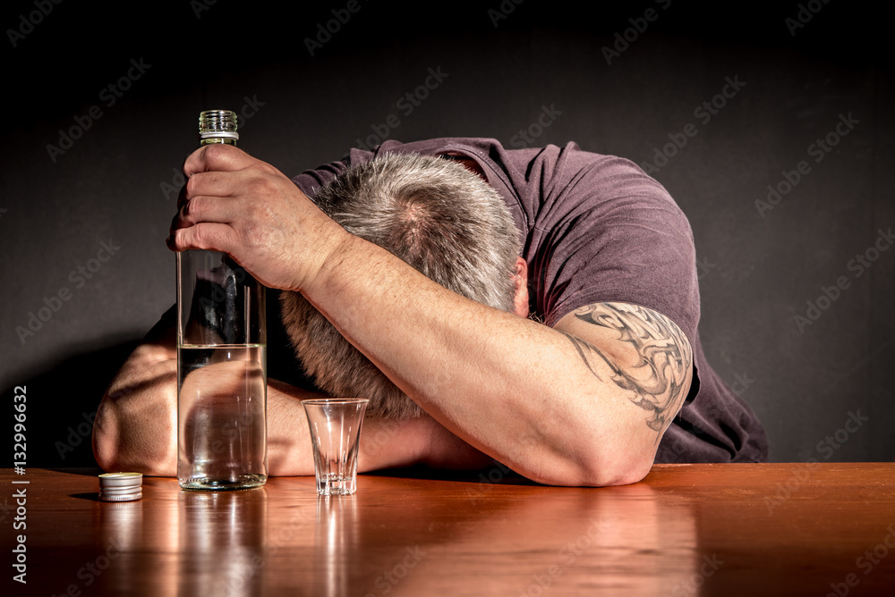 ein Mann sitzt mit einer Flasche Alkohol an einem Tisch - obrazy, fototapety, plakaty 