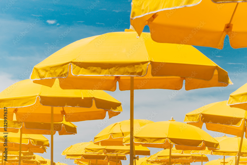 Obraz premium Several yellow umbrellas on the beach against blue sky with clou