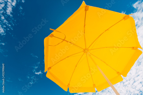 Yellow umbrella on the beach against blue sky with clouds in the