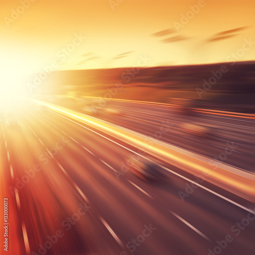 Cars in motion blur on highway at sunset.