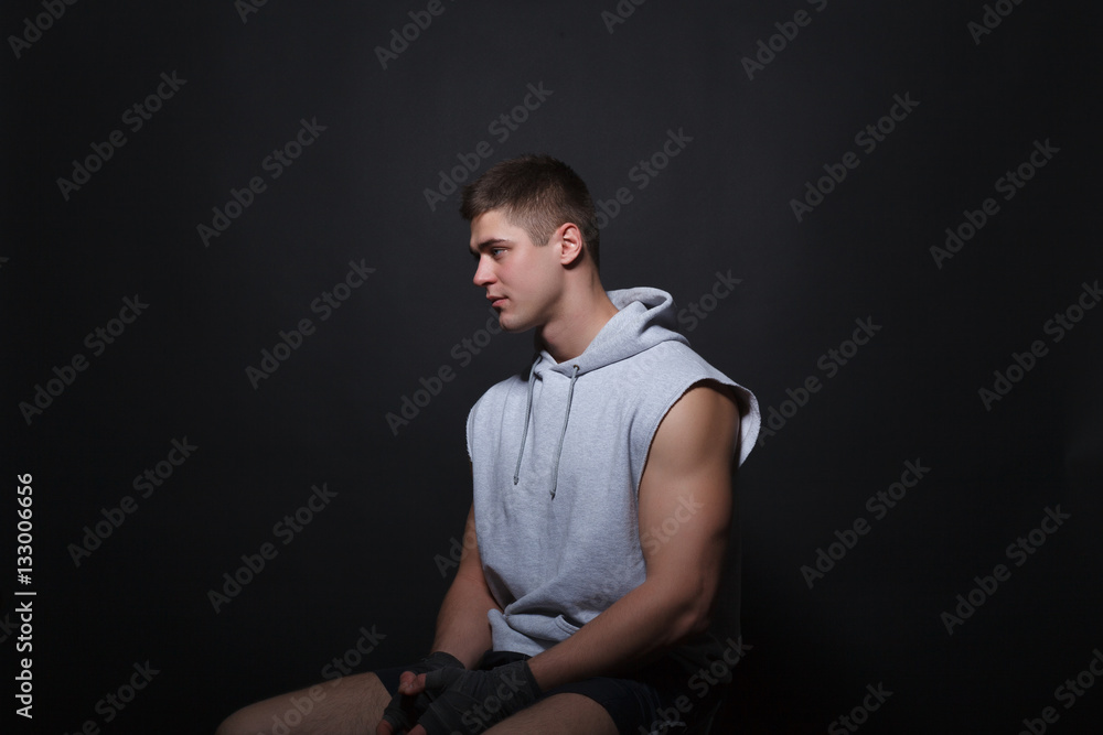 Young muscular boxer sits on a chair on a black background