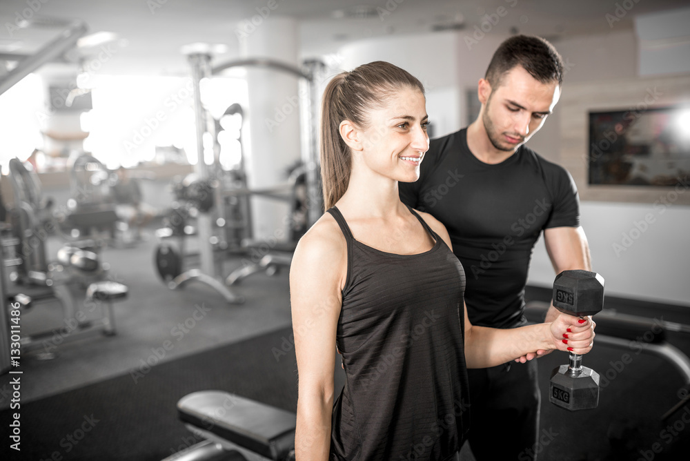Woman doing bicep curls in gym with her personal trainer Woman doing bicep curls in gym with her personal trainer