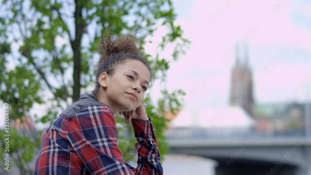 Young woman sitting in urban background and smiling. Young woman sitting in urban background and smiling.