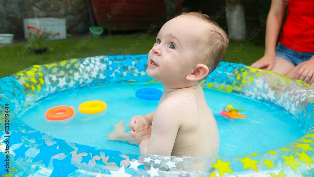Cute baby boy swimming and playing with toys in inflatable pool on grass at garden Cute baby boy swimming and playing with toys in inflatable pool on grass at garden