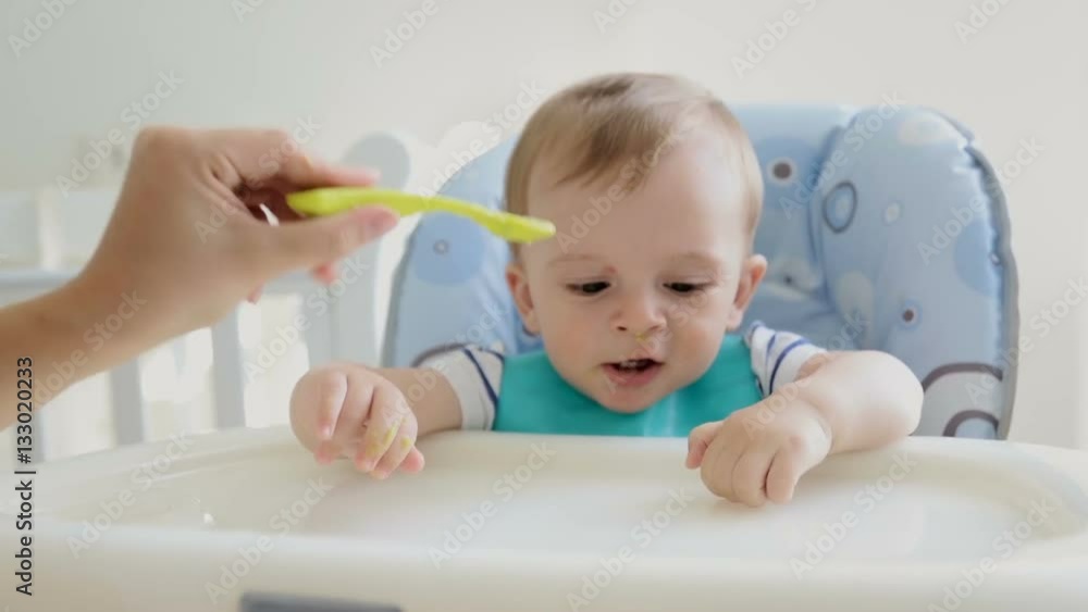 Cheerful baby boy having fun and playing while eating porridge in the highchair Cheerful baby boy having fun and playing while eating porridge in the highchair