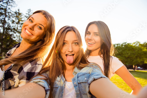 Three happy girls having fun and making comic selfie with tongue