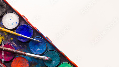 Water color pallet with two paint brushes laying on it with a white background