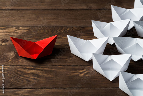 Business leadership concept with white and color paper boats on wooden table